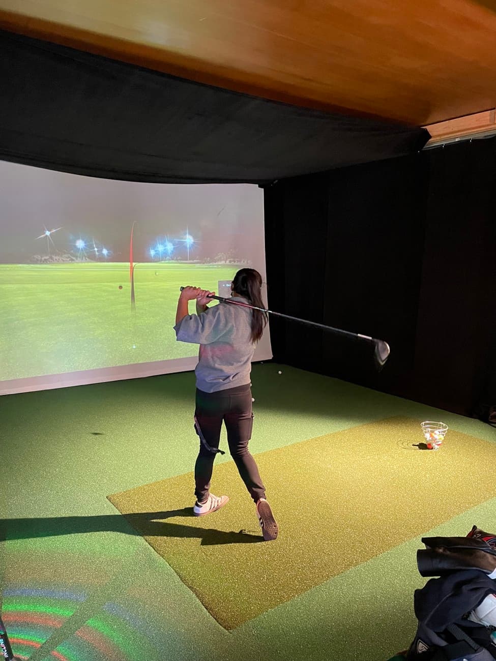 A golfer mid-swing in the indoor TrackMan simulator at Lincoln Park Golf Course in San Francisco