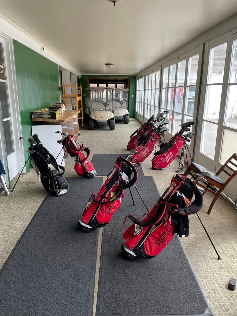 Golf bags lined up in the sunlit clubhouse sunroom at Lincoln Park Golf Course