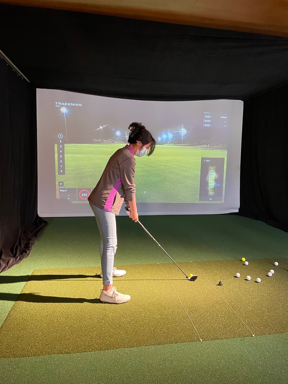 A golfer practicing their swing in the indoor TrackMan simulator at Lincoln Park Golf Course