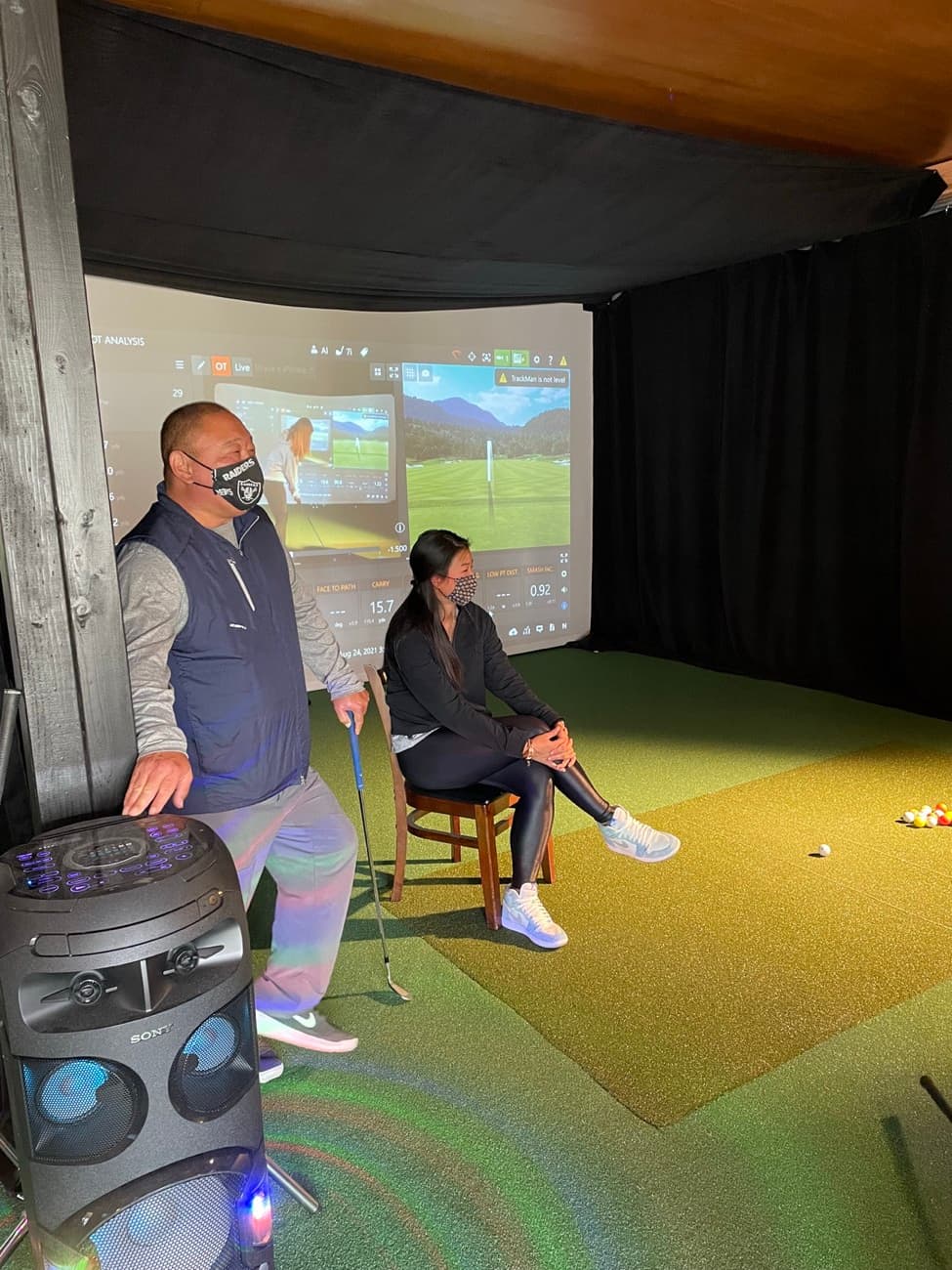 Two golfers practicing in an indoor TrackMan golf simulator bay at Lincoln Park Golf Course