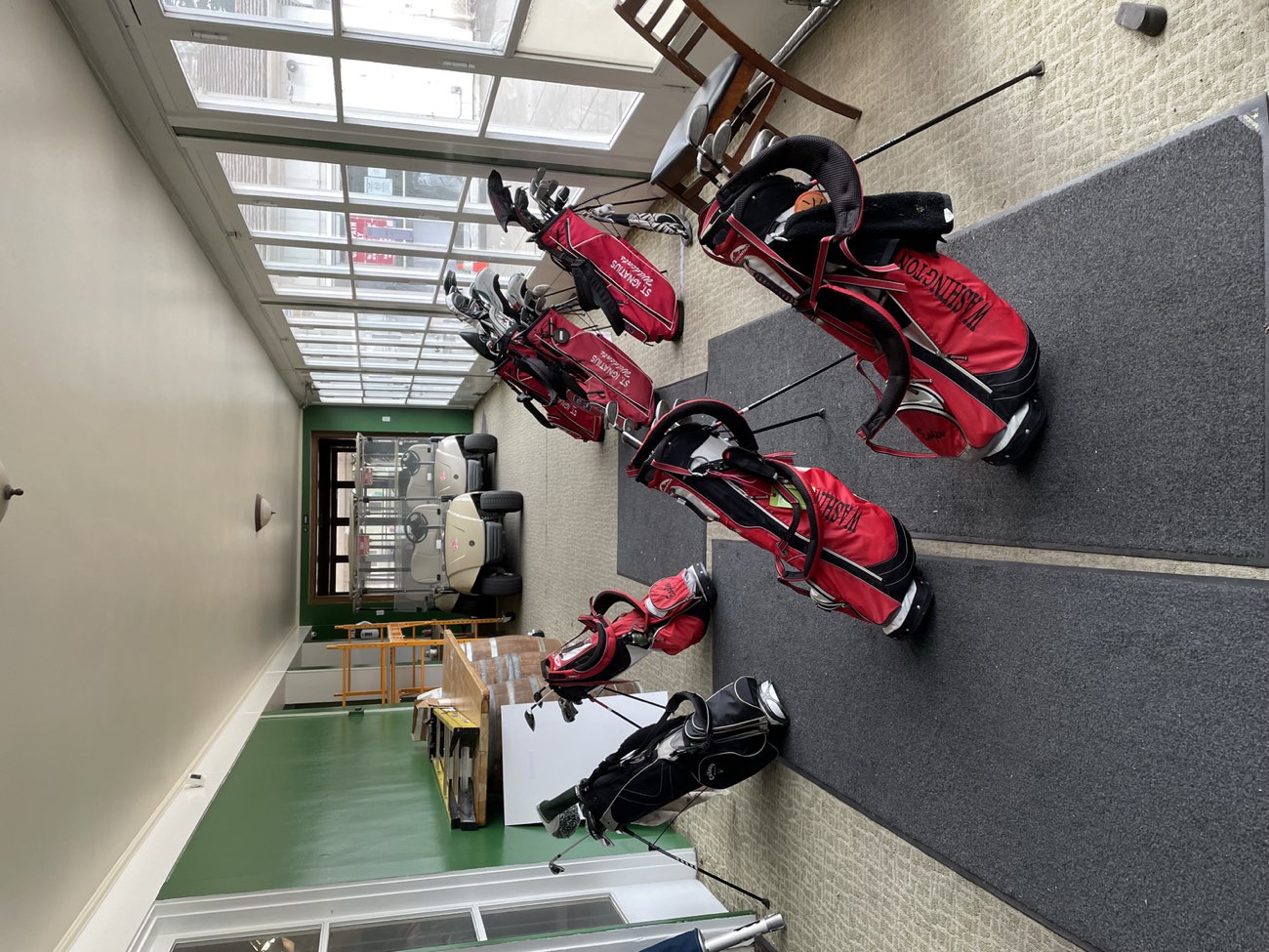 Golf bags lined up in the sunlit clubhouse sunroom at Lincoln Park Golf Course