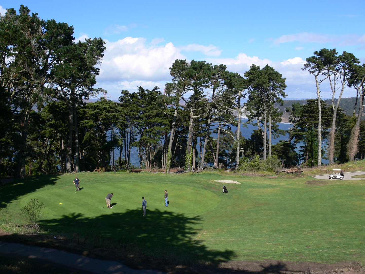 Golfers walking a coastal fairway lined with Monterey cypress at Lincoln Park Golf Course, the Pacific Ocean beyond