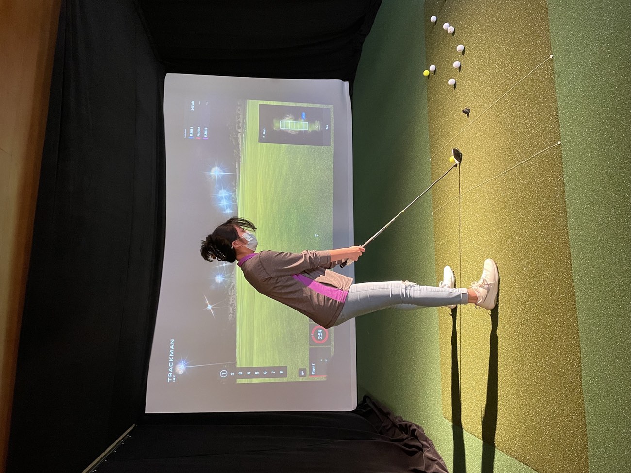 A golfer practicing their swing in the indoor TrackMan simulator at Lincoln Park Golf Course