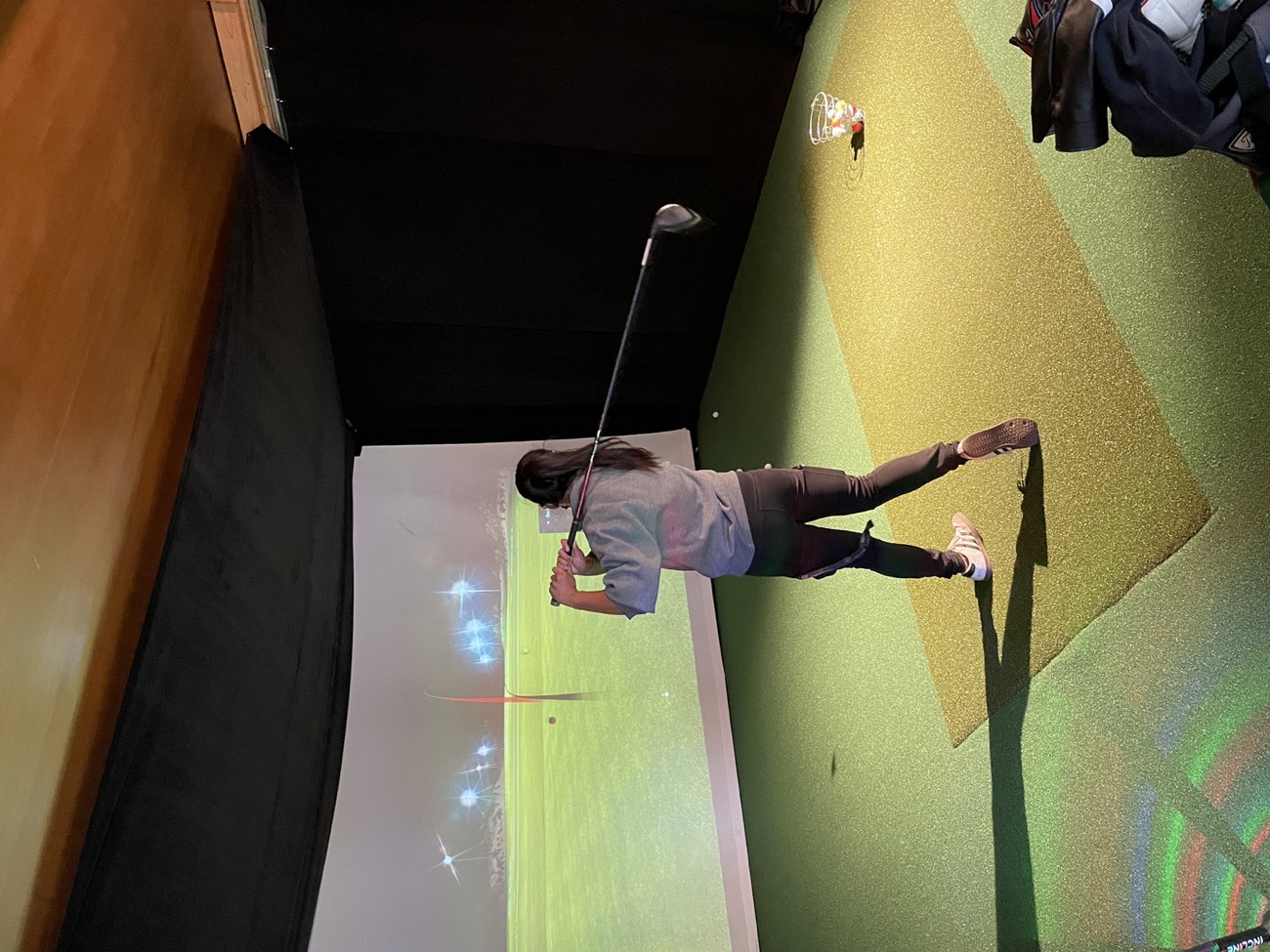 A golfer mid-swing in the indoor TrackMan simulator at Lincoln Park Golf Course in San Francisco