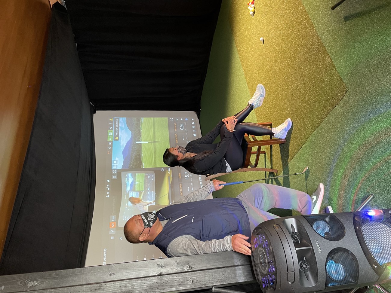 Two golfers practicing in an indoor TrackMan golf simulator bay at Lincoln Park Golf Course